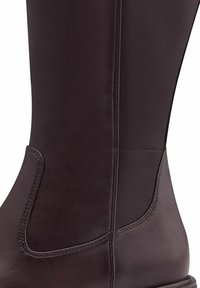 Bota de cuero marrón hasta la rodilla con una textura suave, costuras cosidas y un sutil panel elástico para facilitar su uso.