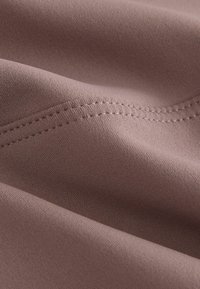 Tessuto morbido e strutturato di colore malva tenue, caratterizzato da linee di cucitura visibili e pieghe sottili. Materiale elastico di alta qualità.
