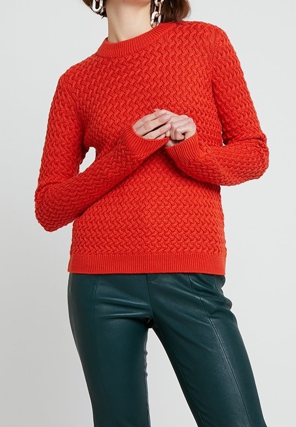Pull en tricot rouge avec un motif texturé, col rond et poignets côtelés, associé à un pantalon en cuir vert.