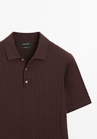 Donkerbruin poloshirt met korte mouwen, voorzien van een gestructureerd kabelgebreid patroon en drie knopen aan de voorkant, gemaakt van 100% katoen.