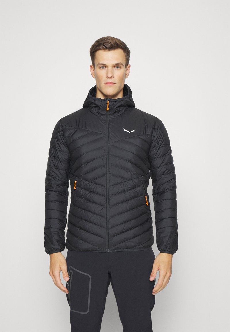 Veste noire isolée avec capuche, présentant un motif matelassé, des zips orange et un logo réfléchissant sur la poitrine. Tissu texturé et léger.