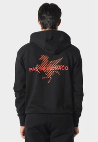 Sudadera con capucha negra que presenta un gráfico a rayas naranjas de un caballo y el texto "PAS DE MONACO" en la parte posterior. Tejido suave, corte relajado.