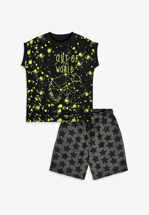 Haut sans manches noir avec ours de constellation jaune néon et texte « Out of the World », associé à un short gris avec motifs d’étoiles noires.