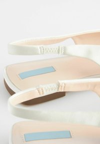 Balti satininiai sandalai su plonomis dirželis, beige pagrindo ir mėlyna stačiakampio akcentu ant vidpadžio. Pasižymi lygiu tekstūra ir minimalistiniu dizainu.