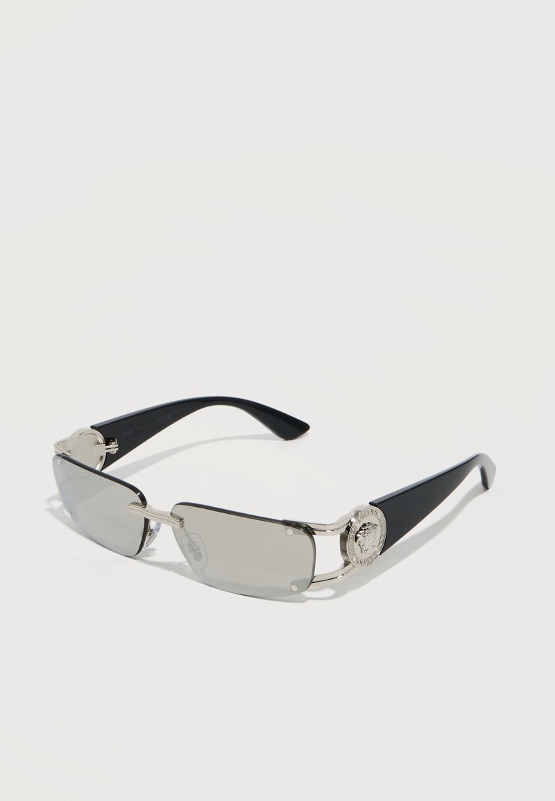 Ορθογώνια γυαλιά ηλίου με γκρι απόχρωση, μαύρους βραχίονες και ασημένιες λεπτομέρειες, με ένα στρογγυλό μενταγιόν σε κάθε πλευρά.