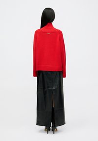 Punainen neulepusero korkealla kauluksella, ribattu yksityiskohta, yhdistettynä mustaan nahkaiseen maksihameeseen, jossa on sivuaukko, käytössä mustat korot.