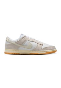 Lavtops Nike sneaker i hvid og beige med tekstureret stof, cremefarvet sål og orange gummiydersål, set fra siden.