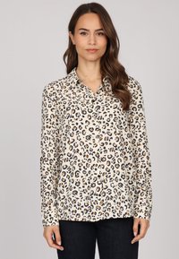 Chemise boutonnée en tissu léger à imprimé léopard, avec une base beige ornée de taches noires et brunes, col pointe et manches longues.