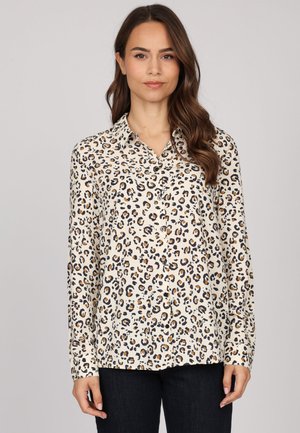 Chemise boutonnée en tissu léger à imprimé léopard, avec une base beige ornée de taches noires et brunes, col pointe et manches longues.