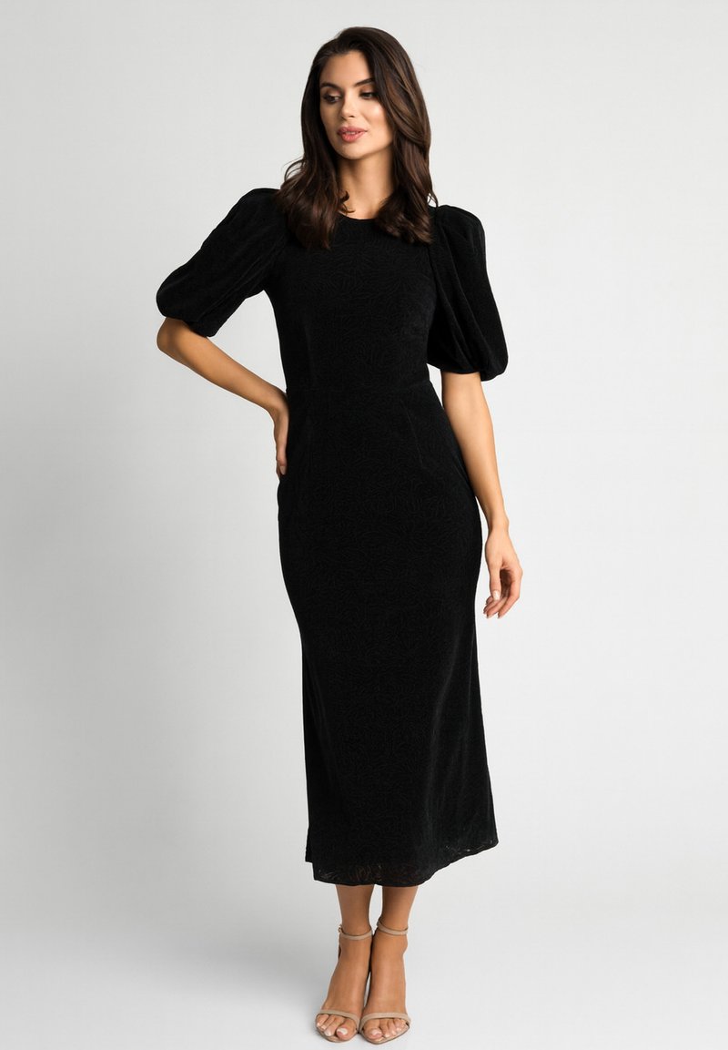 Czarna sukienka midi z bufkami na rękawach, dopasowanym krojem, teksturowaną tkaniną i długością do kolan. Dobraną do niej lekkie sandały na cienkich paskach.