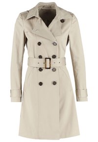 Trench-coat beige à double boutonnage avec large col, ceinture à boucle rectangulaire, poignets boutonnés et poches latérales.