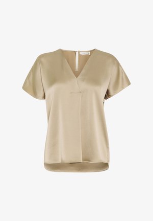 Blouse beige à manches courtes avec un col en V, tissu texturé, couture frontale asymétrique et fermeture éclair partielle au dos.