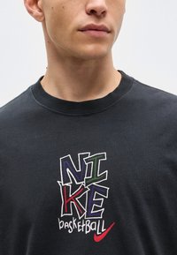 Gros plan d'un homme portant un t-shirt noir avec un texte coloré "NIKE basketball" et un logo Nike swoosh rouge à l'avant.