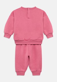 Ροζ φούτερ και παντελόνι σε μαλακό υλικό. Διαθέτει μακριά μανίκια, ριμπ μανσέτες και ελαστική μέση. Η πλάτη έχει μια μικρή λεπτομέρεια ανοιχτού σχεδίου.