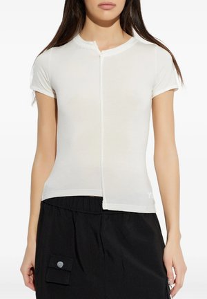 Donna che indossa un top bianco aderente a maniche corte con cucitura frontale e gonna nera con tasca laterale e dettaglio con bottone.