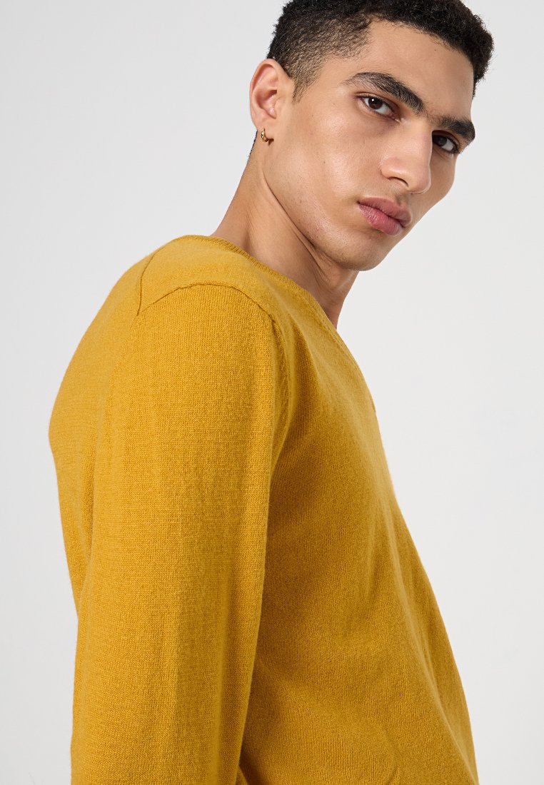 Senapsgul tröja i mjuk stickning, med V-hals, långa ärmar och en avslappnad passform. Subtil struktur framhäver dess utseende.