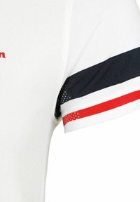 Camisa blanca de manga corta con detalles en rayas azul marino, rojo y blanco en las mangas y una tela texturizada con un logo en rojo.