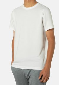 Weißes Kurzarm-T-Shirt aus weicher Baumwolle, mit Rundhalsausschnitt und lockerer Passform. Kombiniert mit grauen strukturierten Hosen.