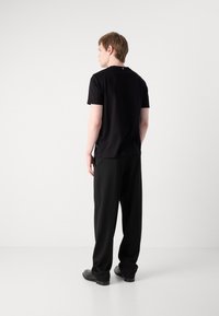 Black cotton t-shirt with a round neckline, short sleeves, and a relaxed fit, paired with loose-fitting black pants and black shoes.