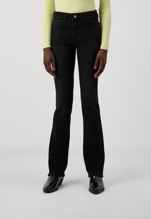 Black flared jeans made from denim with a smooth texture. Worn with a long-sleeve ribbed green top and black heeled boots.