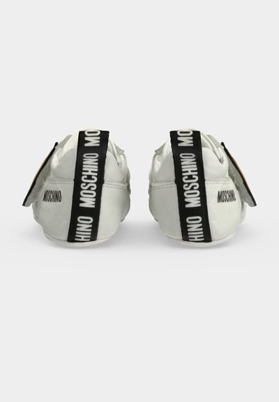 Бели бебешки обувки с марка Moschino, изобразени отзад с черни дръжки с бял надпис Moschino на всеки обувка.