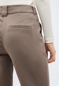 Κοντινό πλάνο ατόμου που φοράει παντελόνι σε καλά ραμμένο ταμπά χρώμα με τσέπη πίσω με φιτίλι και μπεζ ριμπ μπλούζα με μακριά μανίκια.