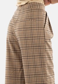 Pantaloni a quadri marroni con design a gamba larga, tessuto testurizzato e una singola tasca posteriore con dettagli di cucitura discreti.