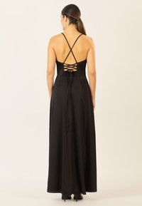 Lang schwarzes Kleid mit satiniertem Finish, ausgestattet mit einem gekreuzten Rücken Design und verstellbaren Schnürungen, bodenlang mit einer fließenden Silhouette.