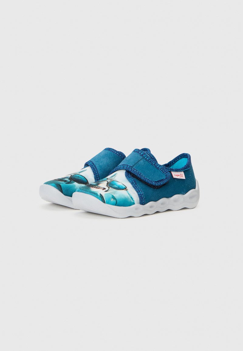 Blaue Slipper mit einem bedruckten Design in verschiedenen Türkistönen. Obermaterial aus Stoff mit einer strukturierten Oberfläche und Klettverschluss. Flexibele weiße Sohle.