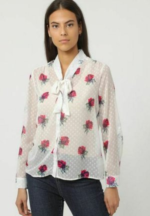 Blusa blanca transparente con lunares y patrones de rosas rojas, con mangas largas, un lazo en el cuello y cierre de botones en la parte delantera.