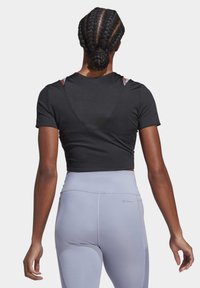 Svart kortärmad sportt-shirt med öppen ryggdesign, parat med ljusgrå högmidjade leggings. Slät tygtextur.