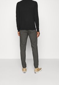 Zwarte trui met lange mouwen, grijze gestructureerde broek en beige sneakers met witte zolen. De outfit heeft een getailleerd ontwerp en neutrale kleuren.