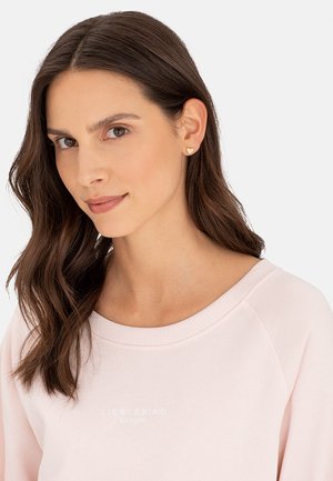 Helles rosa Sweatshirt mit weitem Rundhalsausschnitt, versehen mit geprägtem "LIEBESKIND BERLIN"-Schriftzug und weichem, strukturiertem Stoff, kombiniert mit herzförmigen goldenen Ohrringen.