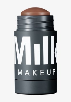 Applicateur en crème brun avec une pointe arrondie, enfermé dans un contenant noir mat comportant un texte blanc en gras.