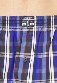 Jockey-rutiga boxers med blå, svart och röd rutmönster, med knäppning och elastisk midja märkt 'Great Since 1876'.