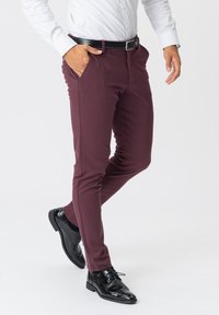 Burgunderfarvede slim-fit bukser lavet af strækbart stof, med sidelommer og lynlås, parret med sorte læderdress sko.