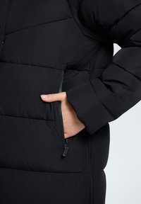 Chaqueta negra acolchada con bolsillo con cremallera, textura suave, patrón acolchado y puños elásticos para calidez y comodidad.