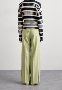 Striped knit sweater in navy, beige, and gray, paired with high-waisted, wide-leg light green trousers featuring side slits.