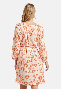 Leopard print dress in cream, featuring shades of orange. Long sleeves with elastic cuffs, cinched waist, and back button detail.