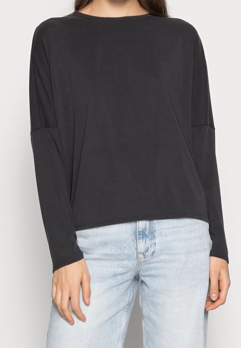 Svart långärmad topp i mjukt tyg med avslappnad passform. Har en rund halsringning och sänkta axlar, tillsammans med ljusa tvättade jeans.