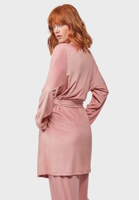 Abito avvolgente rosa pallido con maniche lunghe e vita cinturata, caratterizzato da una consistenza liscia e una vestibilità rilassata. Orlo senza cuciture e silhouette casual.