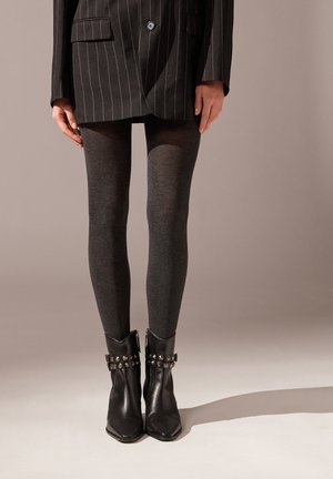 Sort pinstripe blazer, grå uigennemsigtige leggings og sorte ankelstøvler med nittede detaljer og lynlåse. Tætsiddende, slank silhuet.