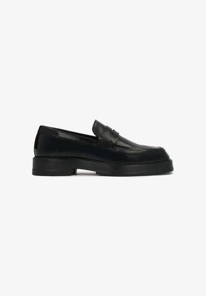 Black leather loafers featuring a smooth finish, raised toe, and a decorative strap across the vamp; thick black rubber sole.