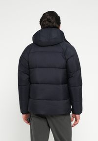 Ciemnogranatowa kurtka puchowa z kapturem, z pikowanymi sekcjami i gładką fakturą. Kurtka ma luźny krój i elastyczne mankiety.
