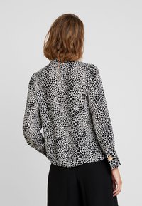 Blouse à manches longues avec un imprimé léopard irrégulier noir et blanc, dotée d'une petite ouverture en forme de clé à l'arrière et d'accents de boutons aux poignets.