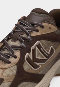 Καφέ και μπεζ αθλητικό παπούτσι Karl Lagerfeld με υφή υφάσματος, επενδύσεις από σουέντ, αντανακλαστικά κορδόνια με ρίγες και λεπτομέρεια λογότυπου στο πλάι.