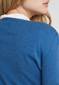 Blå ribbad tröja med rund halsringning och textilstruktur. Bakstycket har en slät design och subtila sömdetaljer.