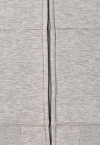 Ljust grå zip-up hoodie gjord av mjukt, texturerat tyg. Har en central dragkedja, ribbade ärmar och nederkant. Enkelt, odekorerat design.