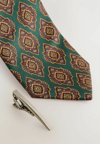Grüne Krawatte mit kunstvollem floralen Muster in Rot, Gold und Blau. Begleitet von einer silbernen Krawattenklammer mit schlichtem Design.