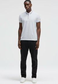 Polo gris clair avec bord noir, patte de boutonnage et texte "CMD SPORT". Associé à un pantalon noir et des baskets blanches.